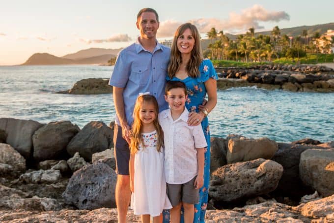 Two adults and two children standing on rocks with a beach in the background.