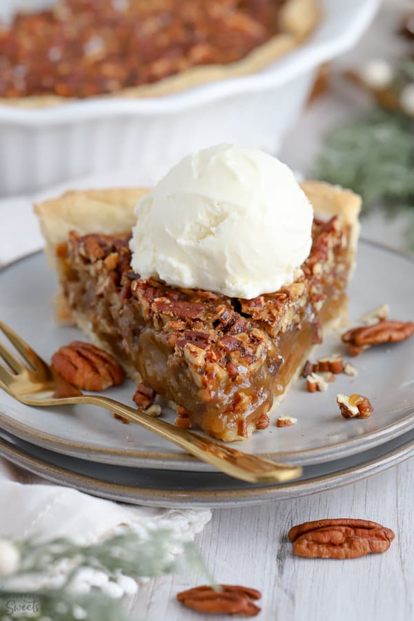 Slice of pecan pie topped with vanilla ice cream on a grey plate.