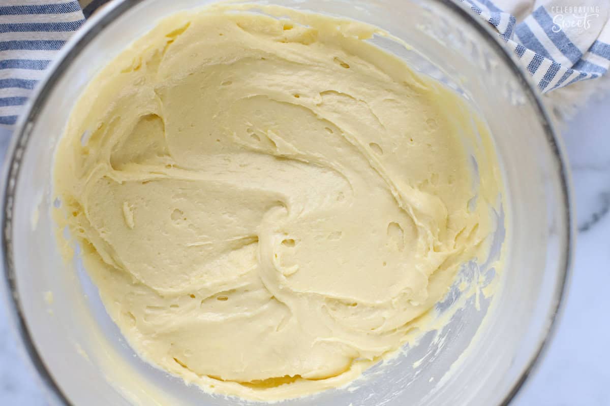 Vanilla cake batter in a glass bowl next to a blue and white striped napkin.