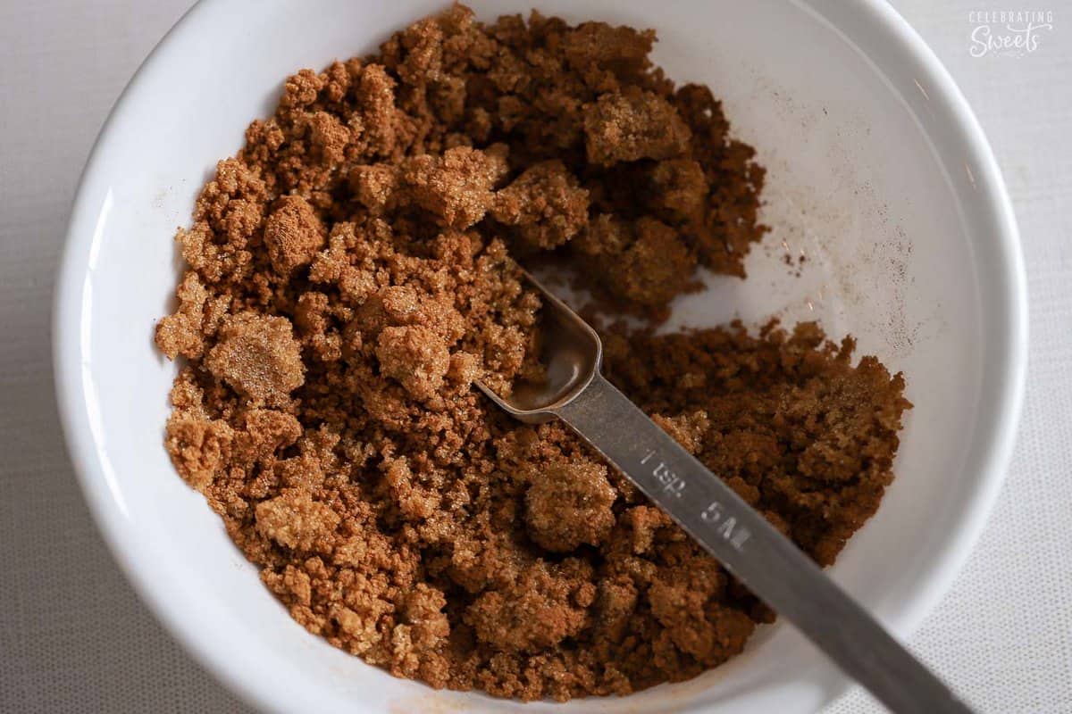 Brown sugar and cinnamon in a  white bowl with a measuring spoon.