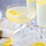 Light yellow French 75 cocktail in a champagne glass topped with a lemon twist.