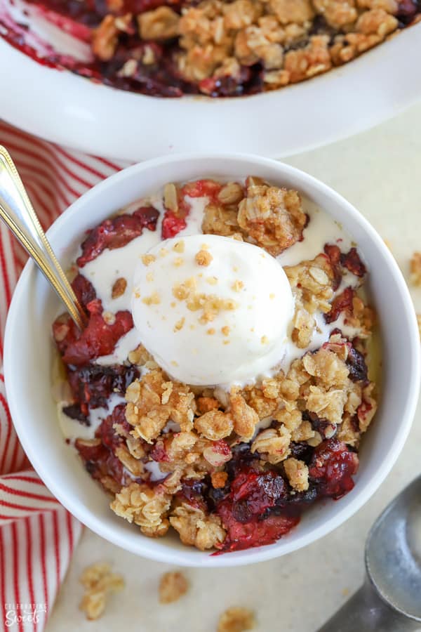 Berry crisp in a white bowl topped with vanilla ice cream.