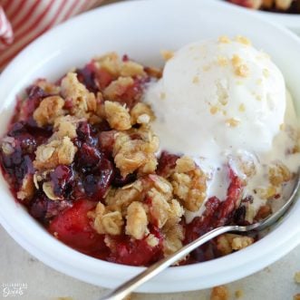 Berry crisp in a white bowl topped with vanilla ice cream.