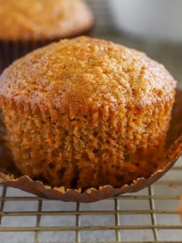 Carrot muffin in a brown wrapper on a wire rack