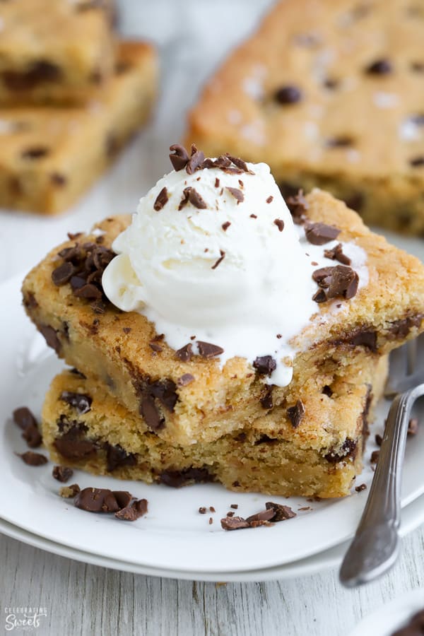Two chocolate chip cookies bars on a white plate with a scoop of vanilla ice cream on top.