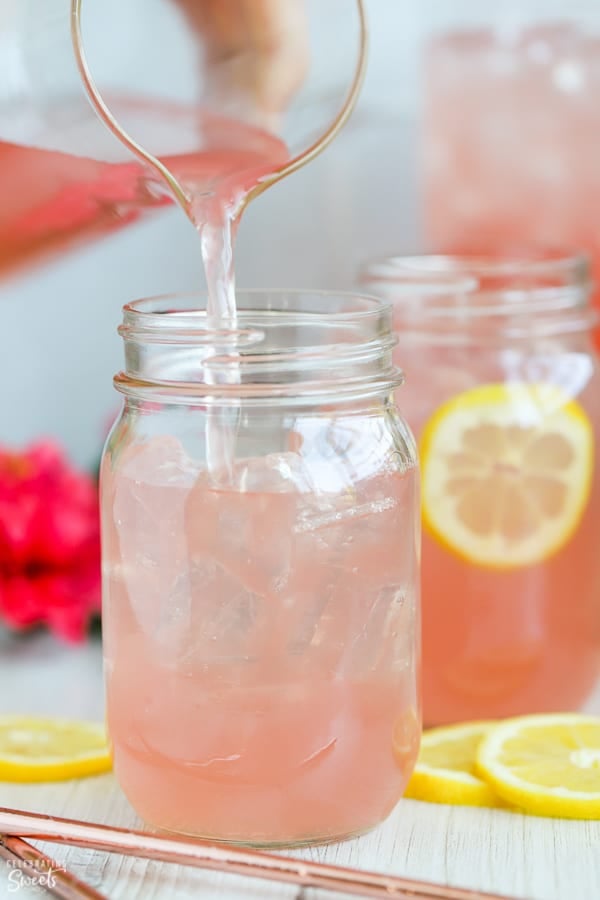 Pink lemonade being poured into a mason jar filled with ice. 