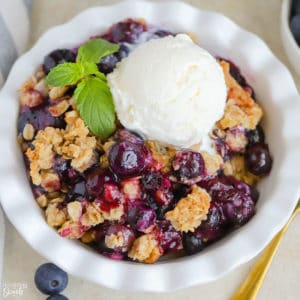 Blueberry Crisp topped with ice cream in a white bowl.