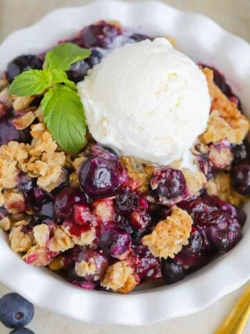 Blueberry Crisp topped with ice cream in a white bowl.