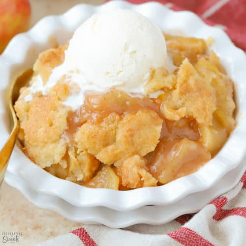 Apple cobbler in a white dish topped with vanilla ice cream.