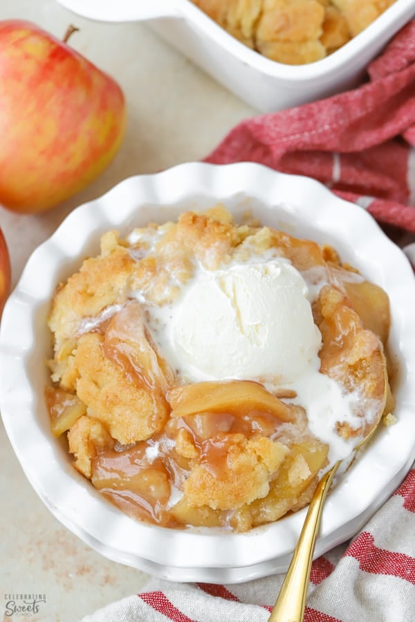 Apple cobbler in a white dish topped with vanilla ice cream.