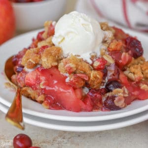 Scoop of Apple Cranberry Crisp topped with vanilla ice cream on a white plate.