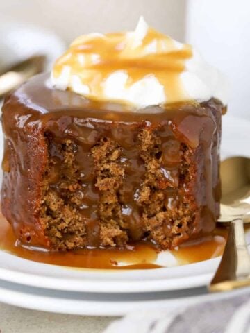 Sticky toffee pudding cake on a white plate topped with whipped cream.