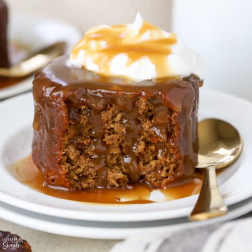 Sticky toffee pudding cake on a white plate topped with whipped cream.