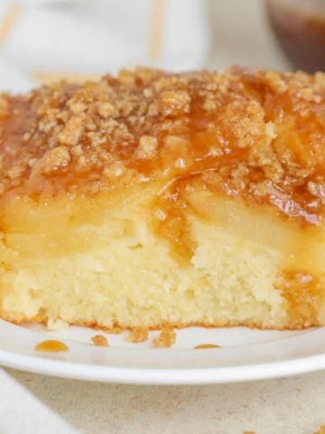 Slice of pineapple cake topped with crumble and brown sugar sauce on a white plate