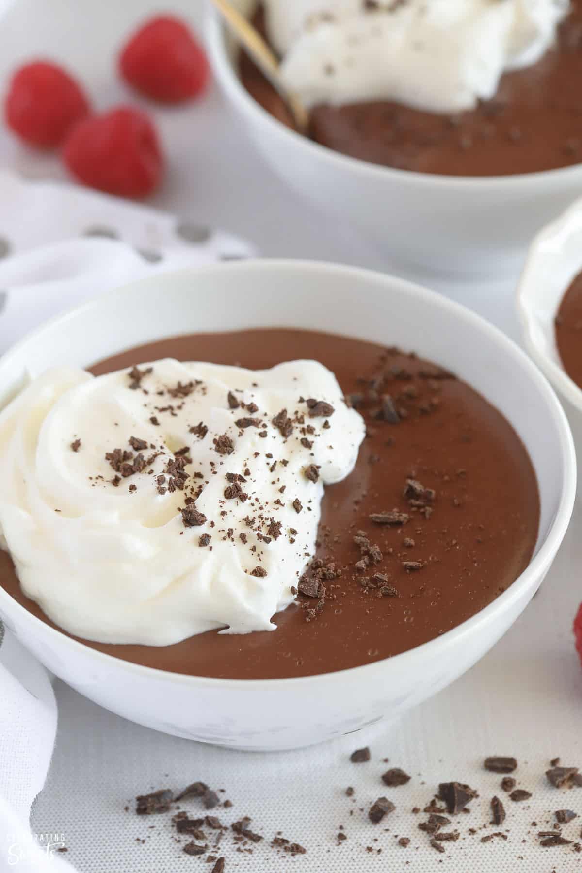 Closeup of chocolate pudding in a white bowl topped with chopped chocolate and whipped cream
