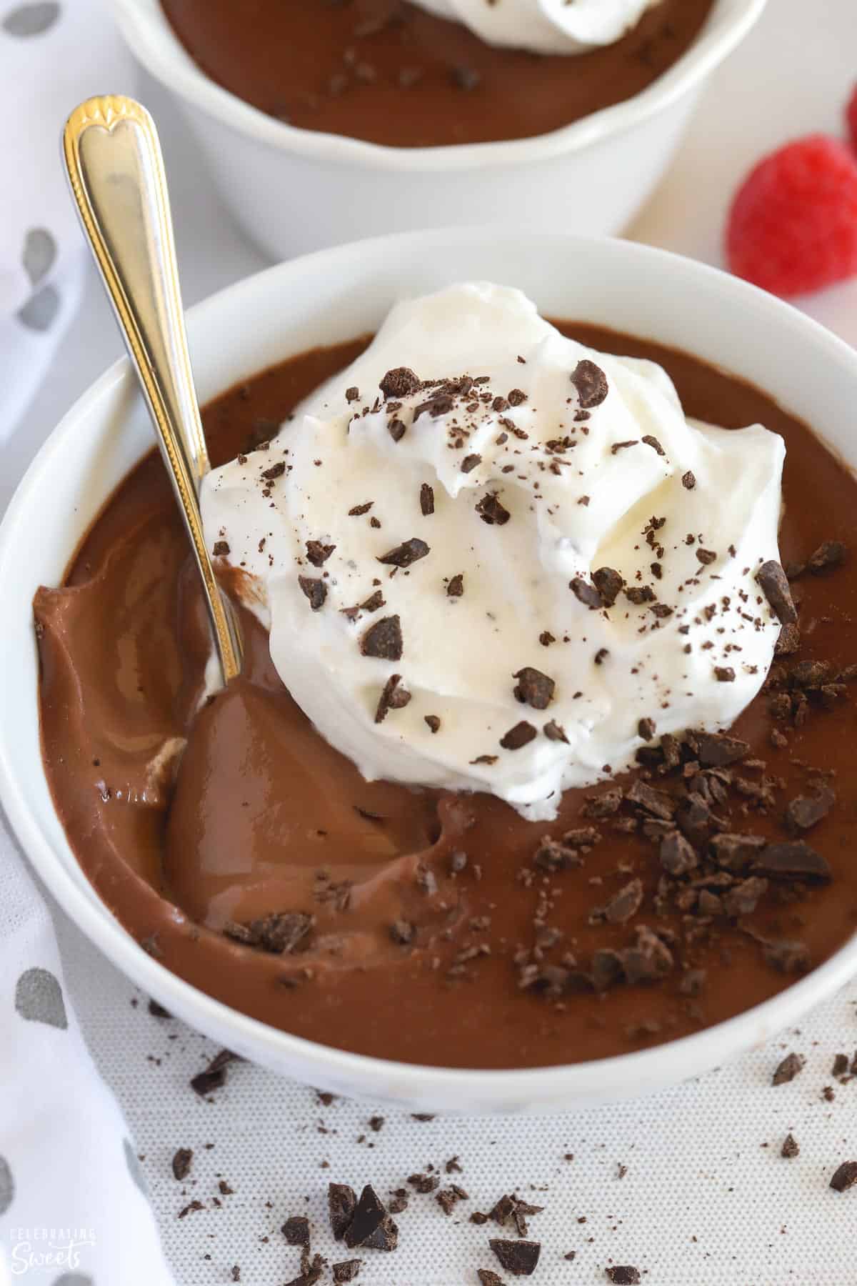 Closeup of chocolate pudding in a white bowl topped with chopped chocolate and whipped cream