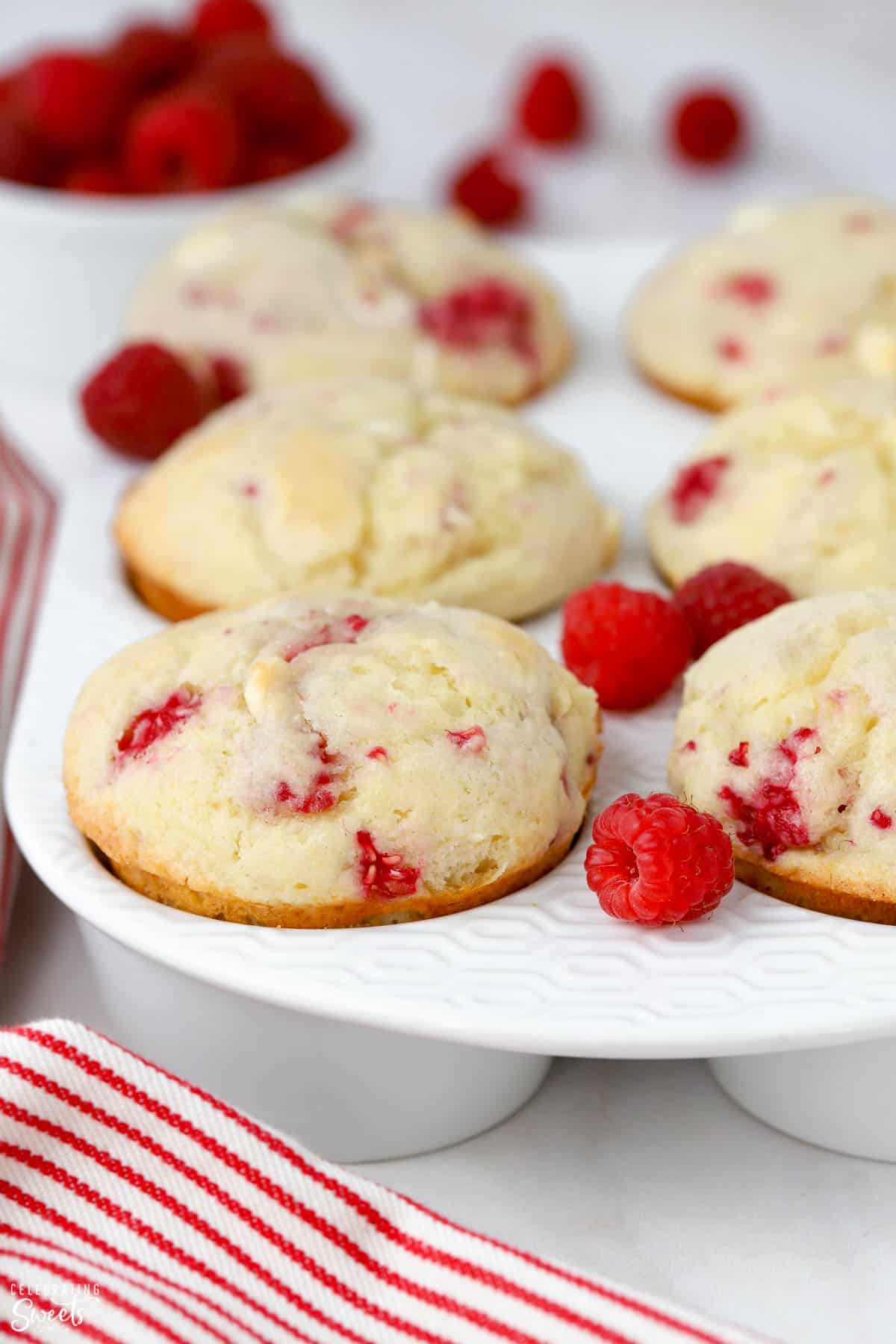 Raspberry muffins in a white baking dish surrounded by fresh raspberries.