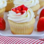 Closeup of vanilla cupcake topped with white frosting and fresh strawberries.
