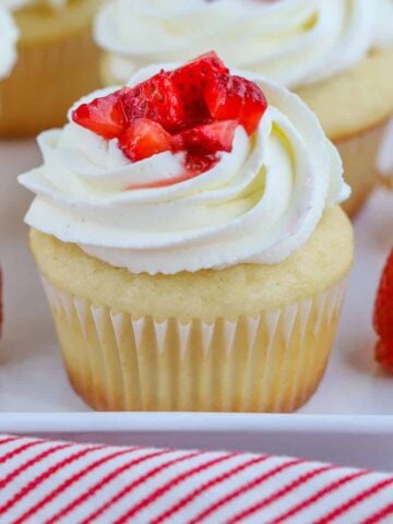 Closeup of vanilla cupcake topped with white frosting and fresh strawberries.