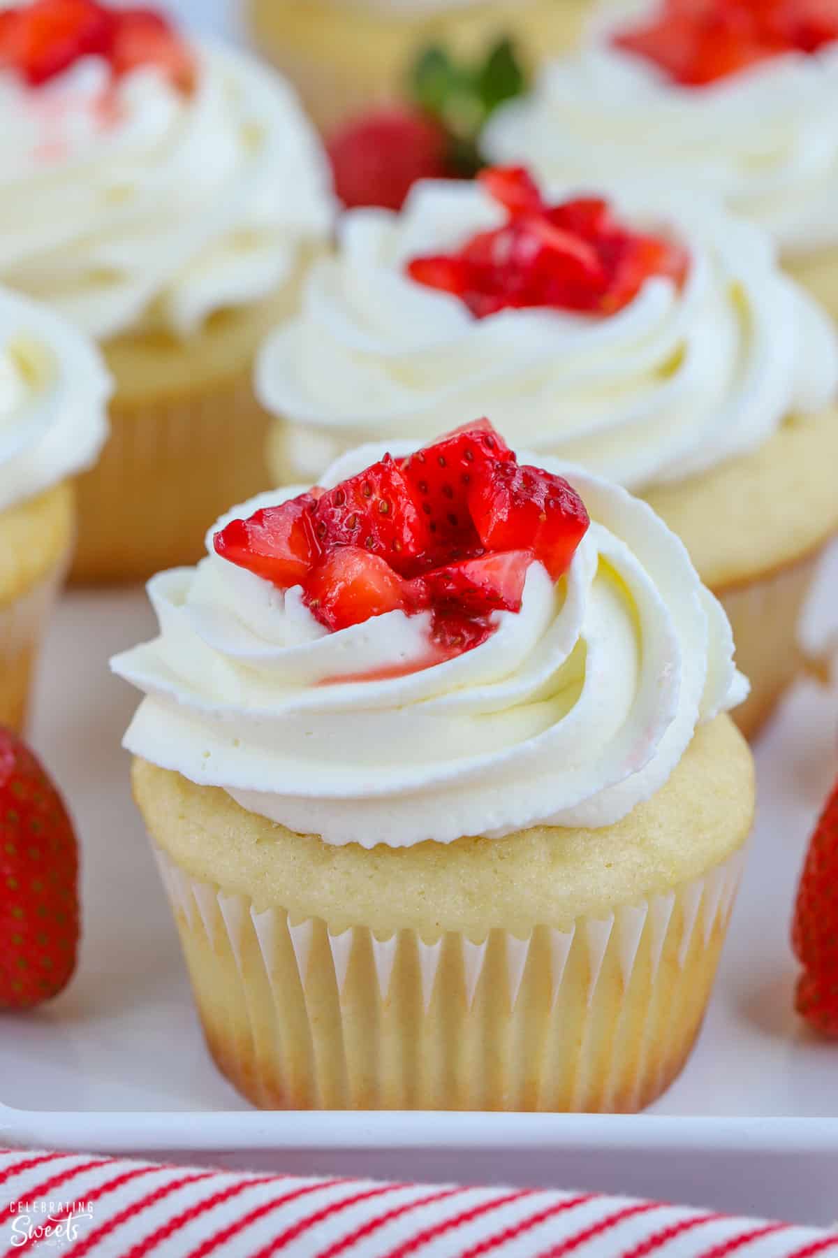 Closeup of vanilla cupcake topped with white frosting and fresh strawberries.