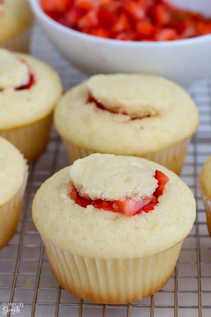 Vanilla cupcakes on a wire rack with strawberry filling inside.