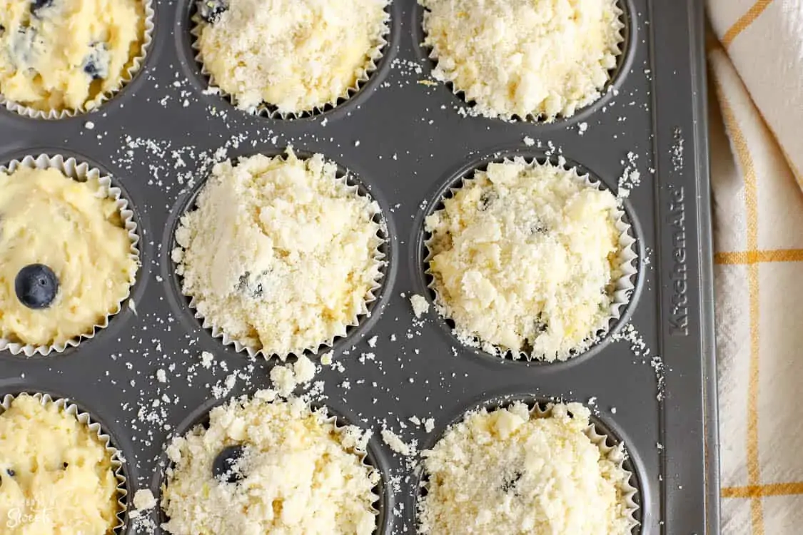 Muffin batter in a muffin tin topped with crumb topping.