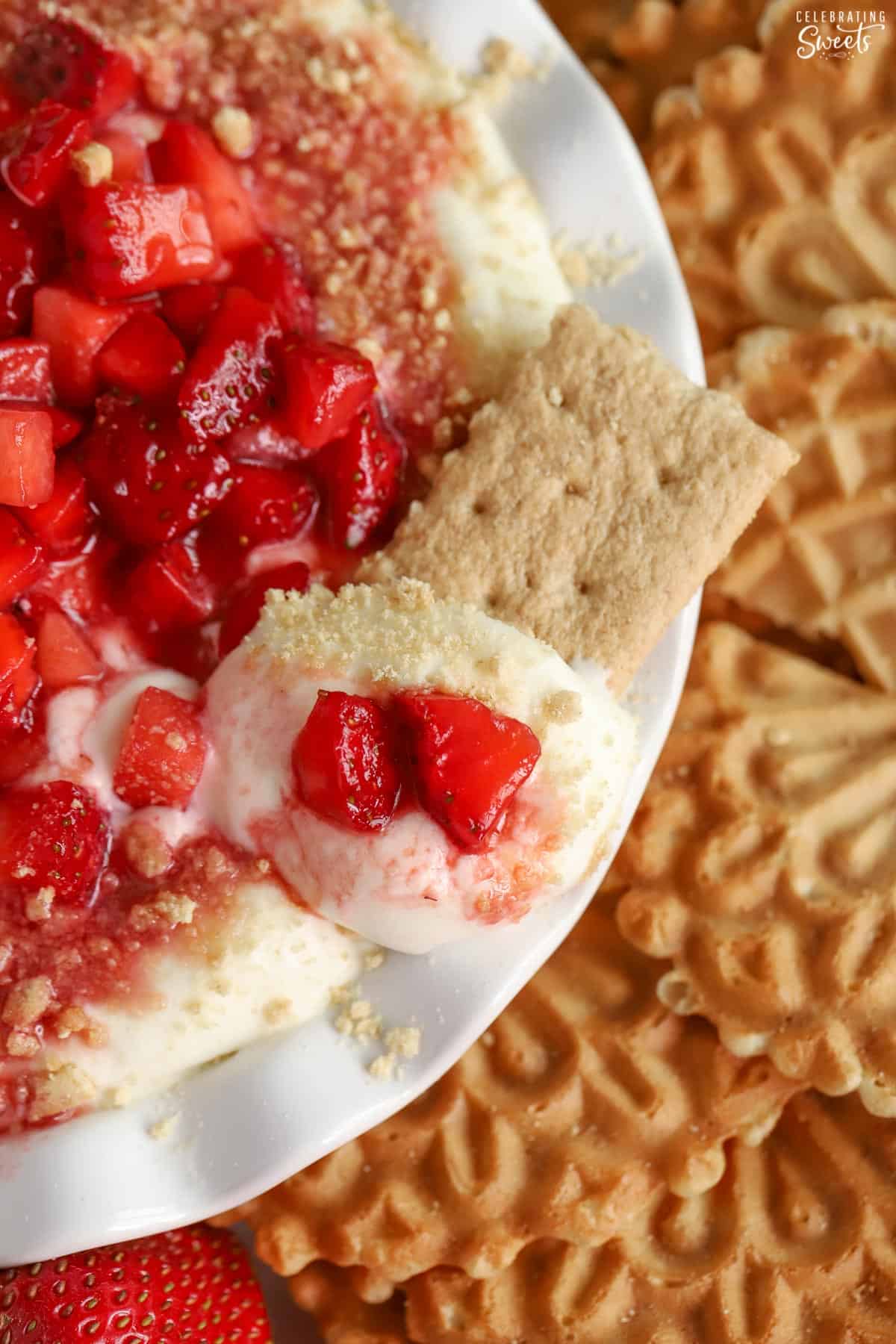 Cheesecake dip in a white bowl topped with strawberries with a graham cracker in it