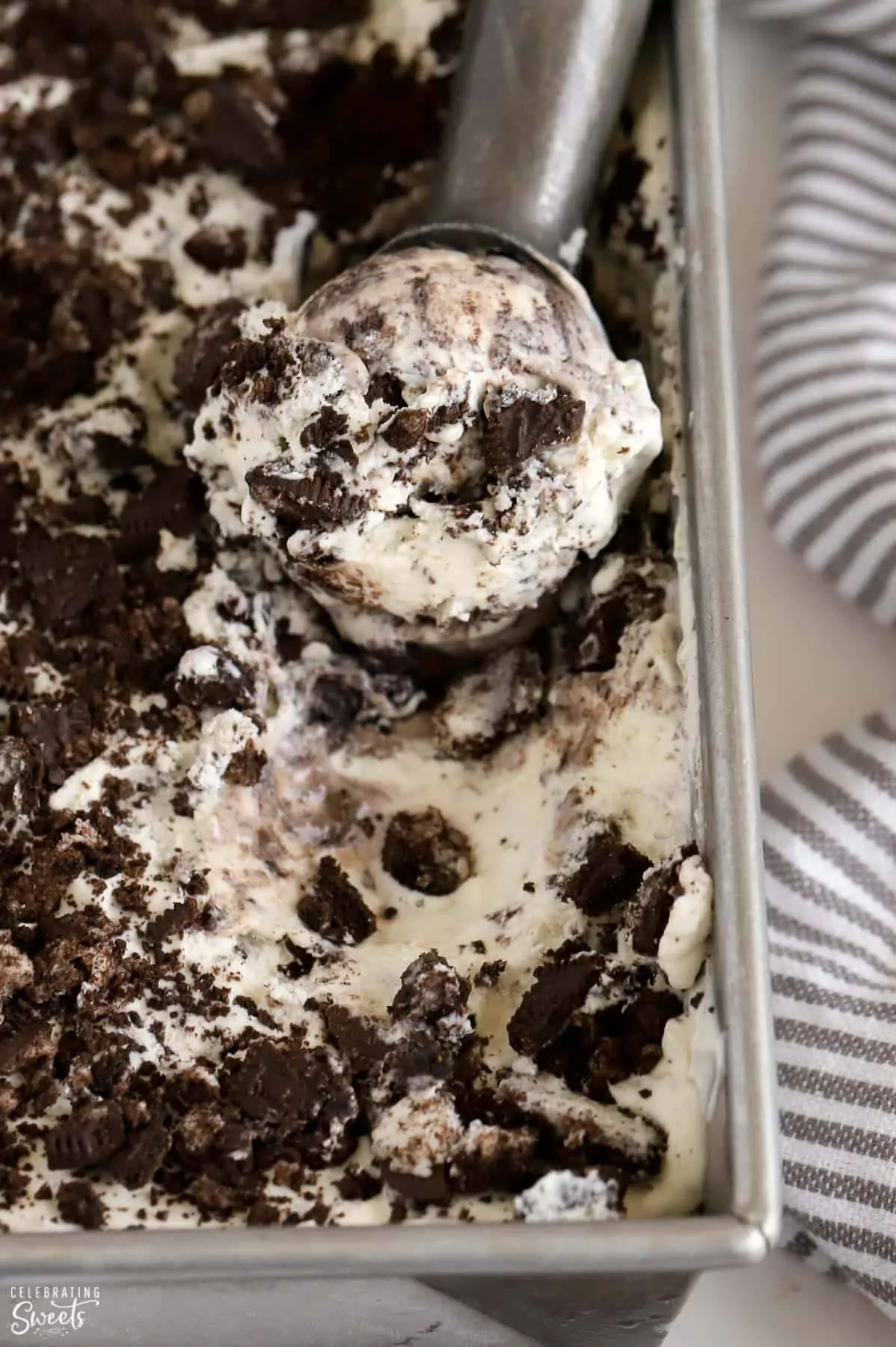 Cookies and cream ice cream in a loaf pan with a silver ice cream scoop.