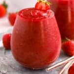 Dark red Frosé wine slushies in a glass garnished with strawberries.