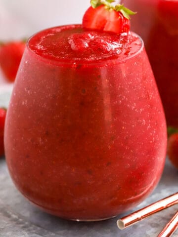 Dark red Frosé wine slushies in a glass garnished with strawberries.