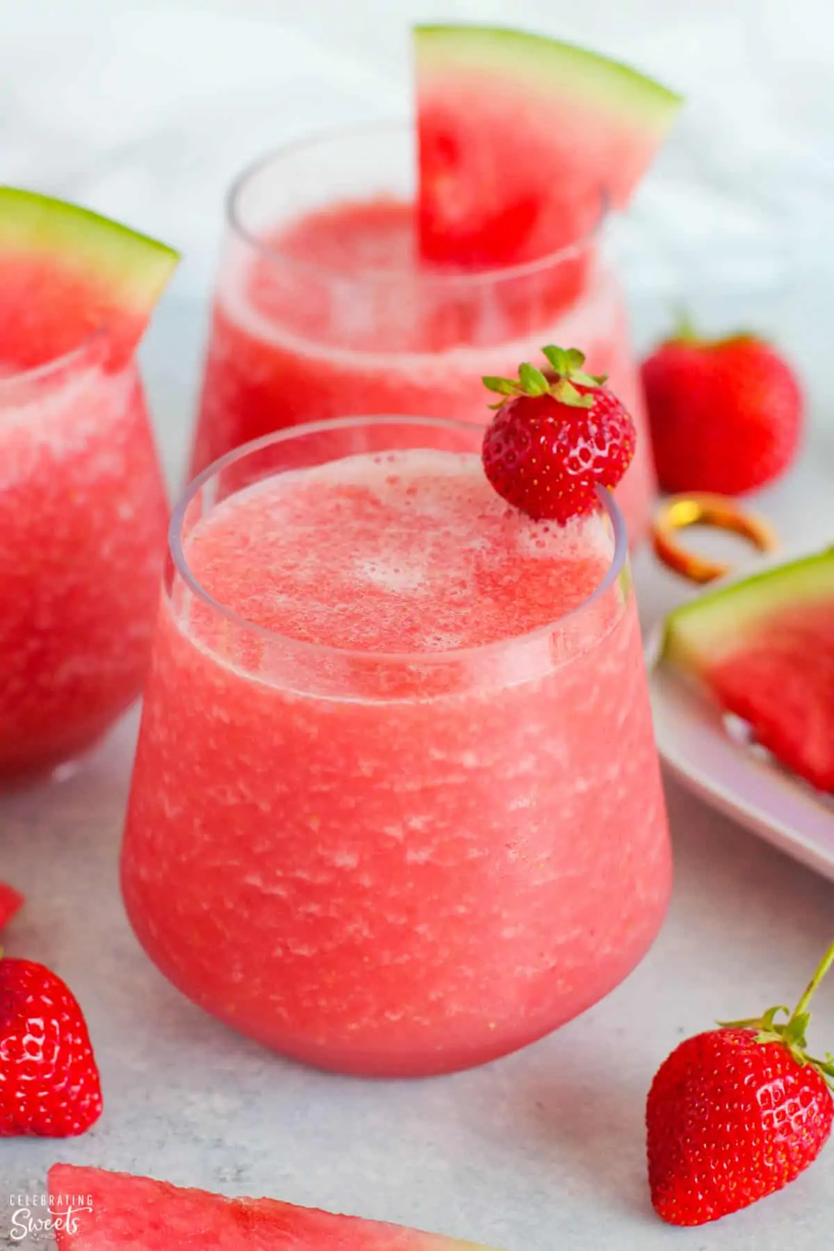 Pink Frosé wine slushies in a glass garnished with strawberries and watermelon.