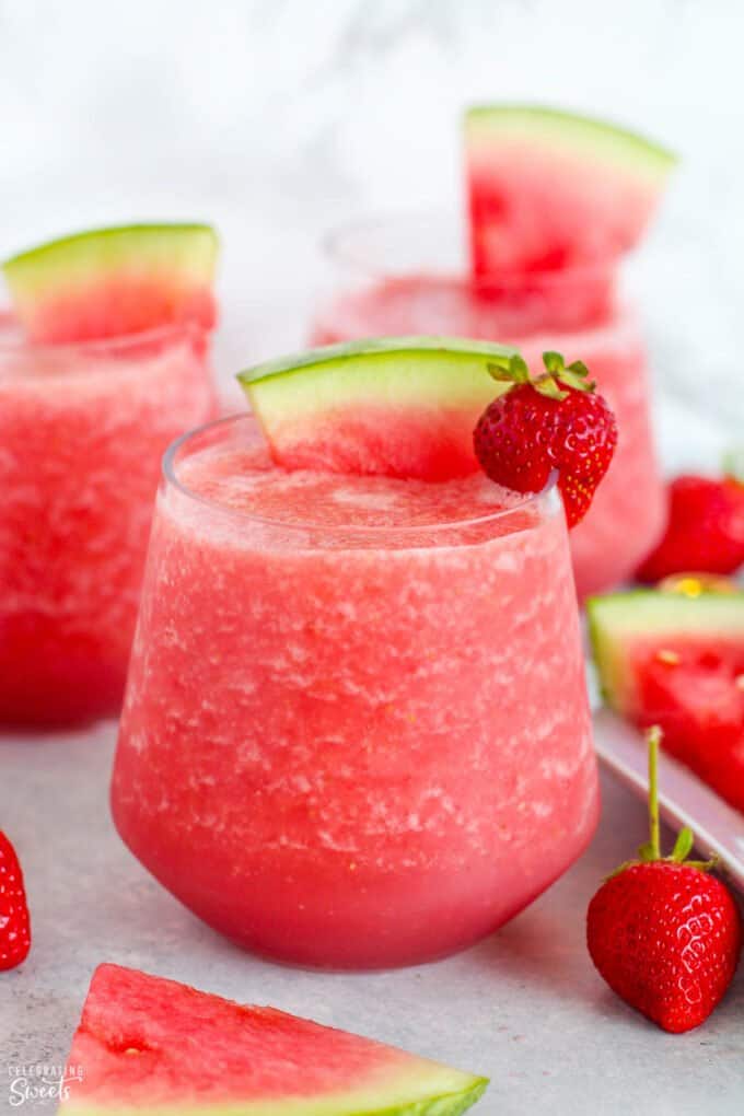 Pink Frosé wine slushies in a glass garnished with strawberries and watermelon.