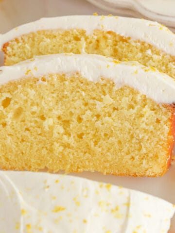 Two slices of lemon loaf cake topped with frosting and lemon zest.