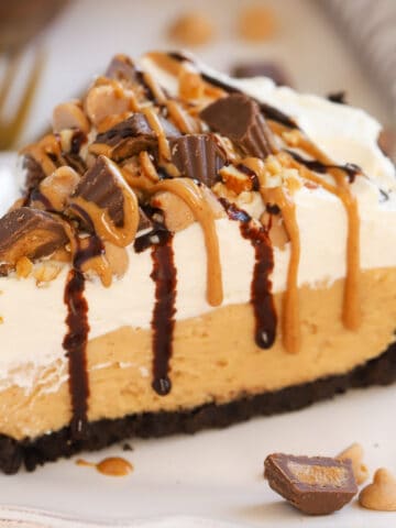 Slice of peanut butter pie topped with chopped peanut butter cups and drizzled with fudge sauce and peanut butter.