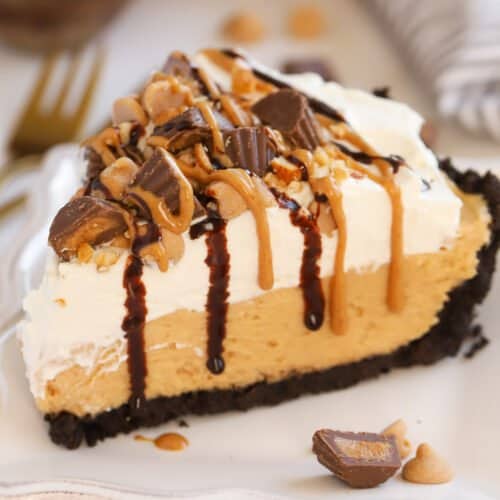 Slice of peanut butter pie topped with chopped peanut butter cups and drizzled with fudge sauce and peanut butter.