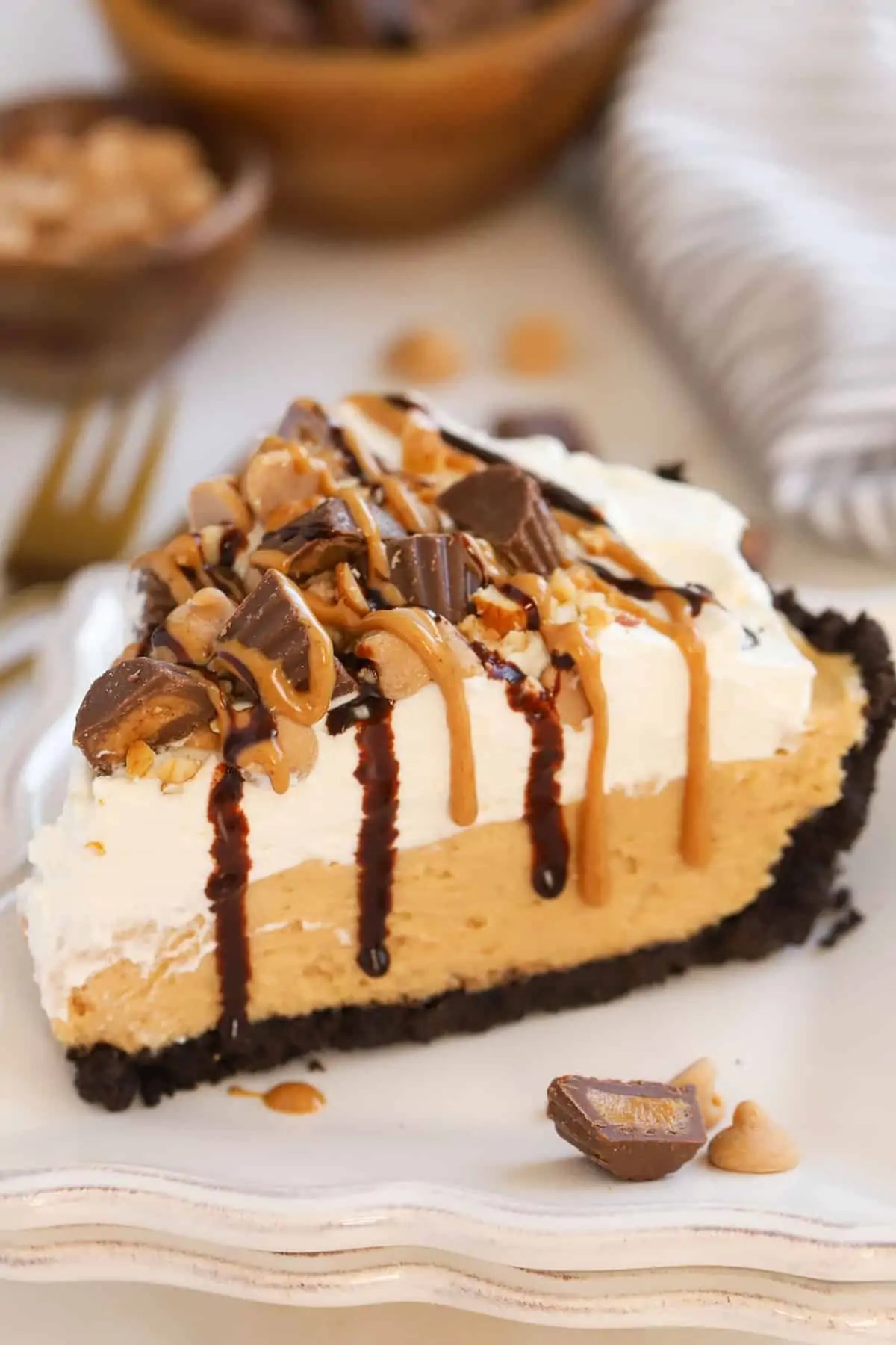 Slice of peanut butter pie topped with chopped peanut butter cups and drizzled with fudge sauce and peanut butter.