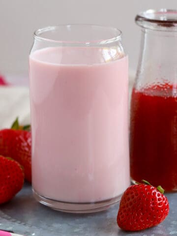 Glass of strawberry milk and a carafe of strawberry syrup.