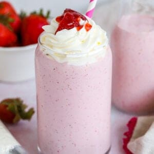 Strawberry milkshake in a glass topped with whipped cream and strawberries.