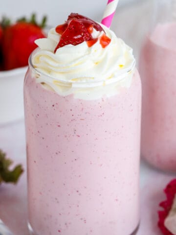 Strawberry milkshake in a glass topped with whipped cream and strawberries.