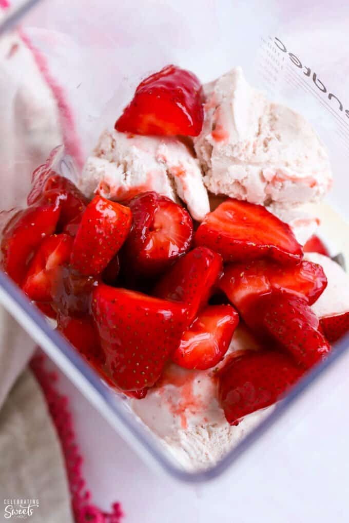 Strawberries and ice cream in the bowl of a blender.