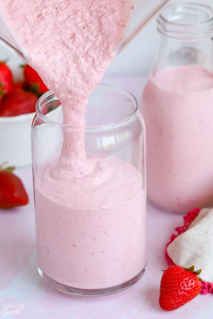 Strawberry milkshake being poured into a glass.