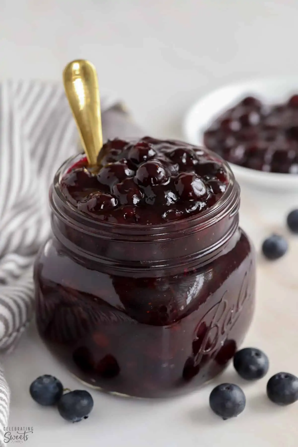 Blueberry Pie Filling in a glass jar with a gold spoon.