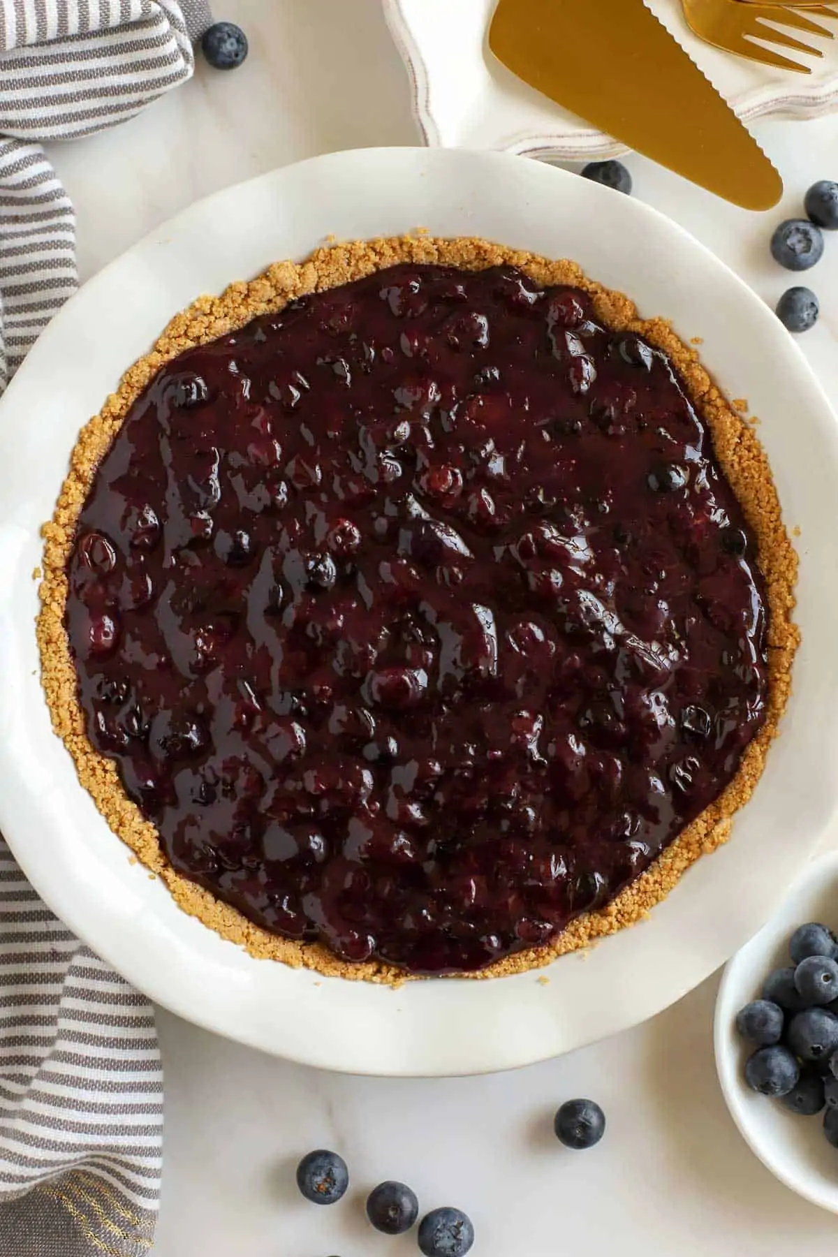 Blueberry pie filling in a graham cracker crust surrounded by fresh blueberries.