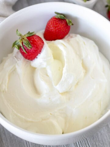 Whipped cream in a white bowl with strawberries.