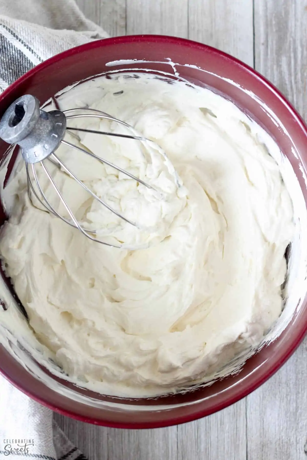 Homemade whipped cream in a red bowl with a stainless beater.