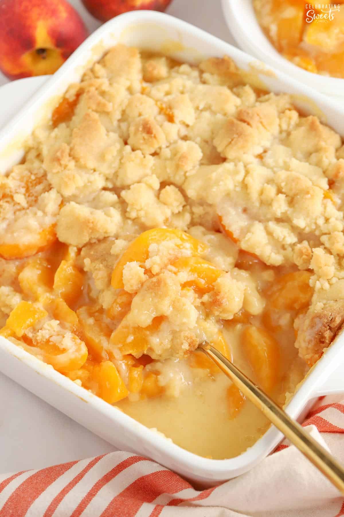 Peach Cobbler in a white baking dish with a gold spoon.