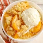 Peach Cobbler in a white bowl topped with a scoop of vanilla ice cream.