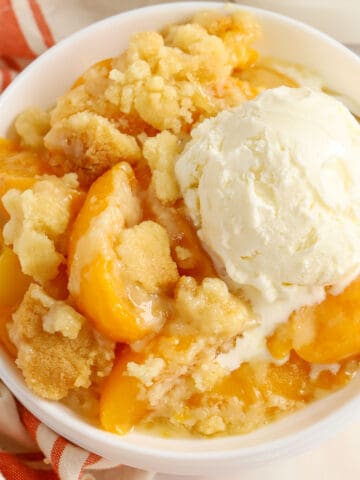 Peach Cobbler in a white bowl topped with a scoop of vanilla ice cream.