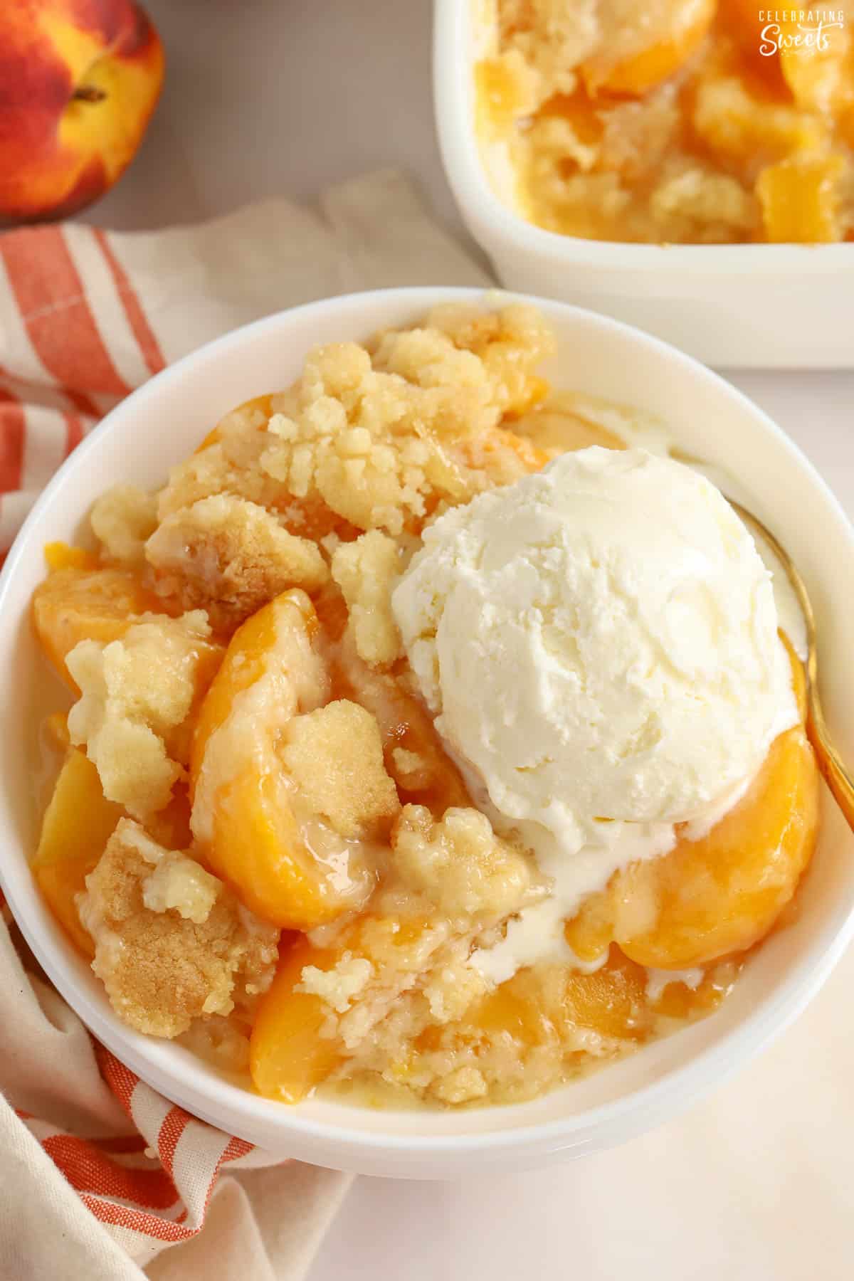Peach Cobbler in a white bowl topped with a scoop of vanilla ice cream.