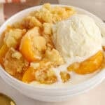 Peach cobbler in a white bowl topped with ice cream.
